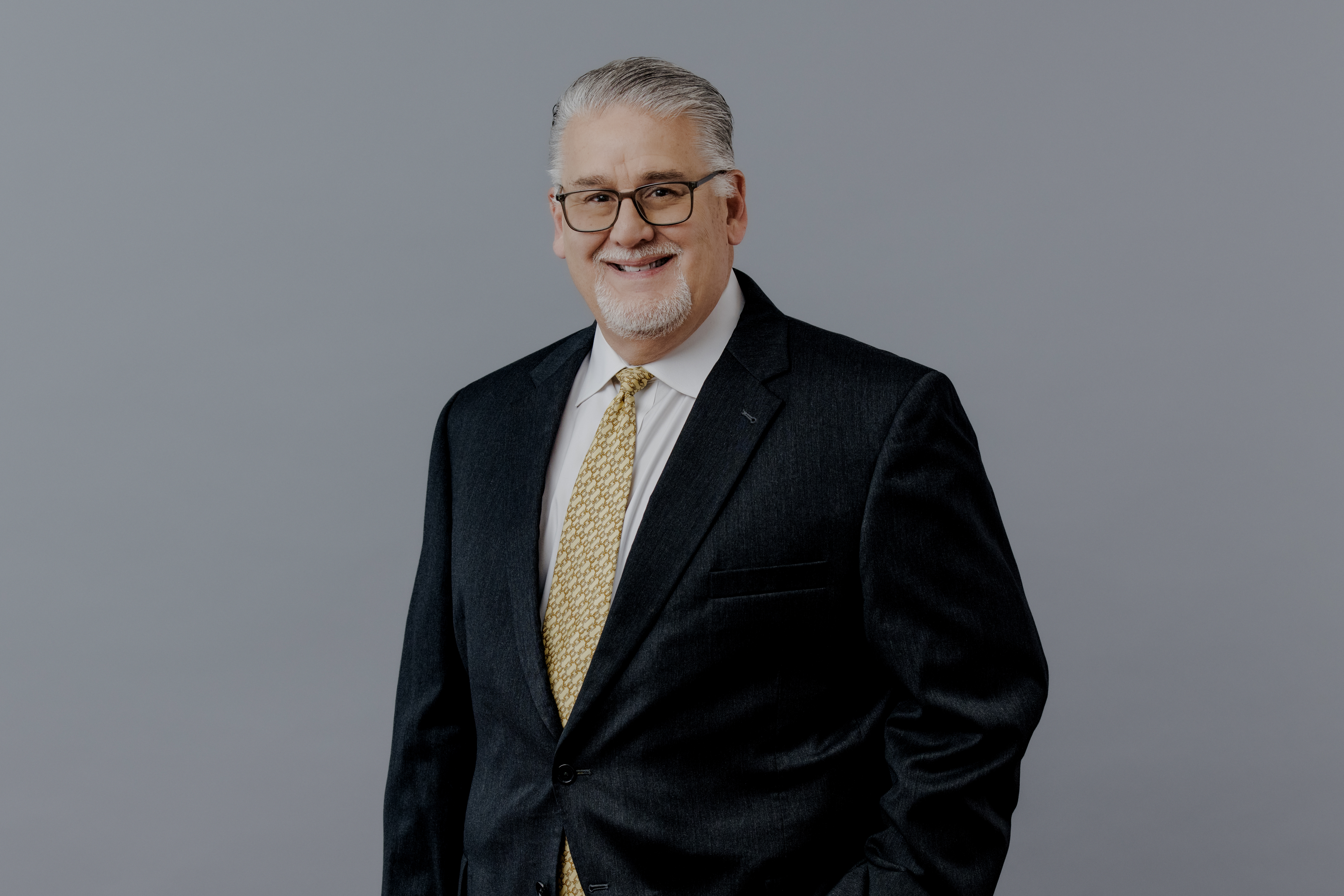 Headshot of a businessman in a suit and tie in front of gray backdrop. 