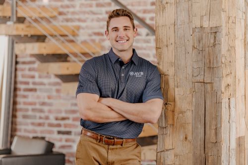 Man in casual business attire leaning on wooden post. 