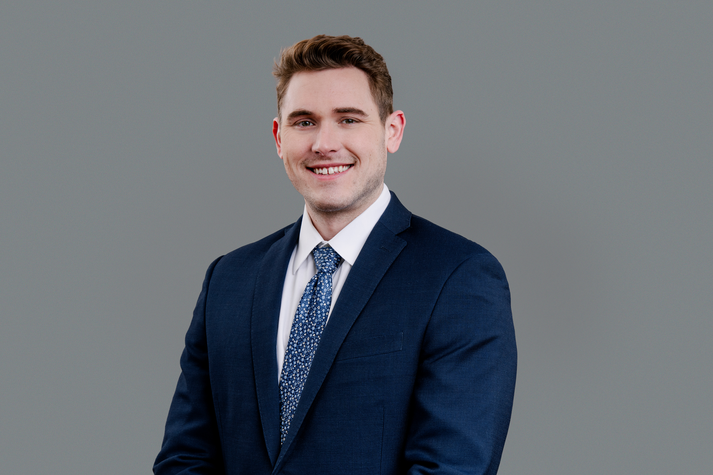 Man in blue business suit and tie in front of gray background. 